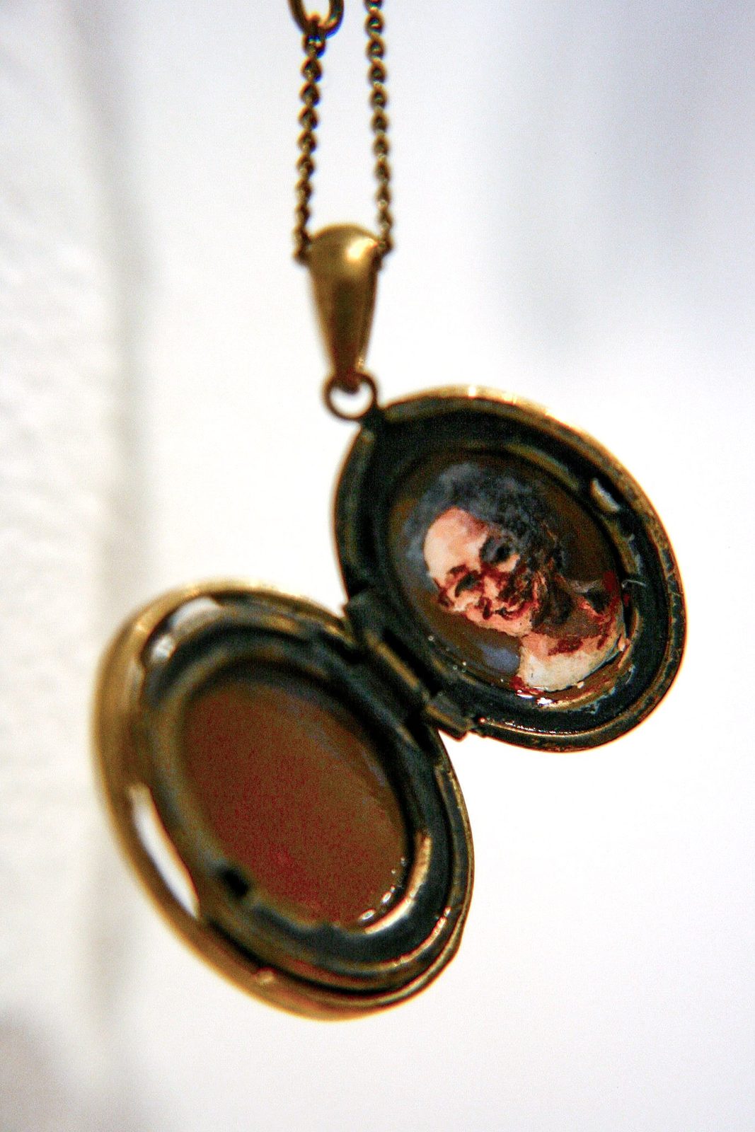 Open bronze oval locket on a chain holding a small painted portrait of a woman's face.